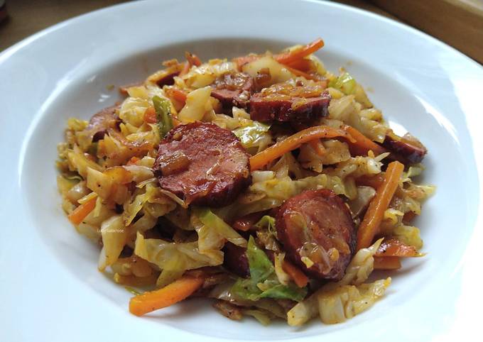 A picture of Sautéed cabbage and carrot with sausage.