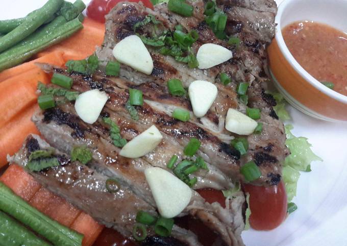 A picture of Moo Kam Waan / Thai style Grilled Pork serve with Spicy Sauce and fresh vegetables.