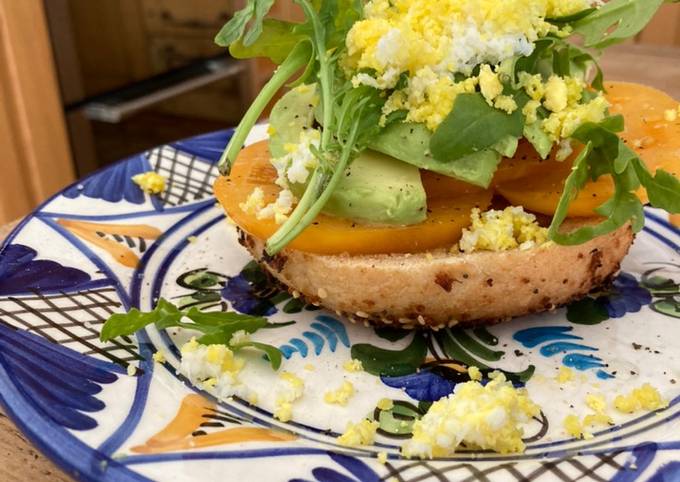 A picture of Tomato and avocado on toasted bagel with grated egg.