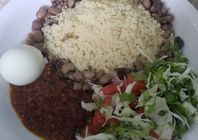 A picture of Cooked couscous and beans with sauce and vegetables.