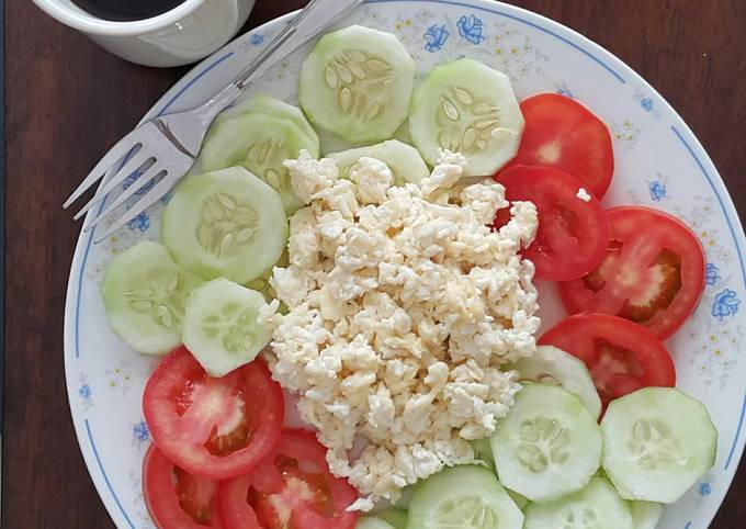 A picture of Scrambled eggs with tomato and cucumber salad.